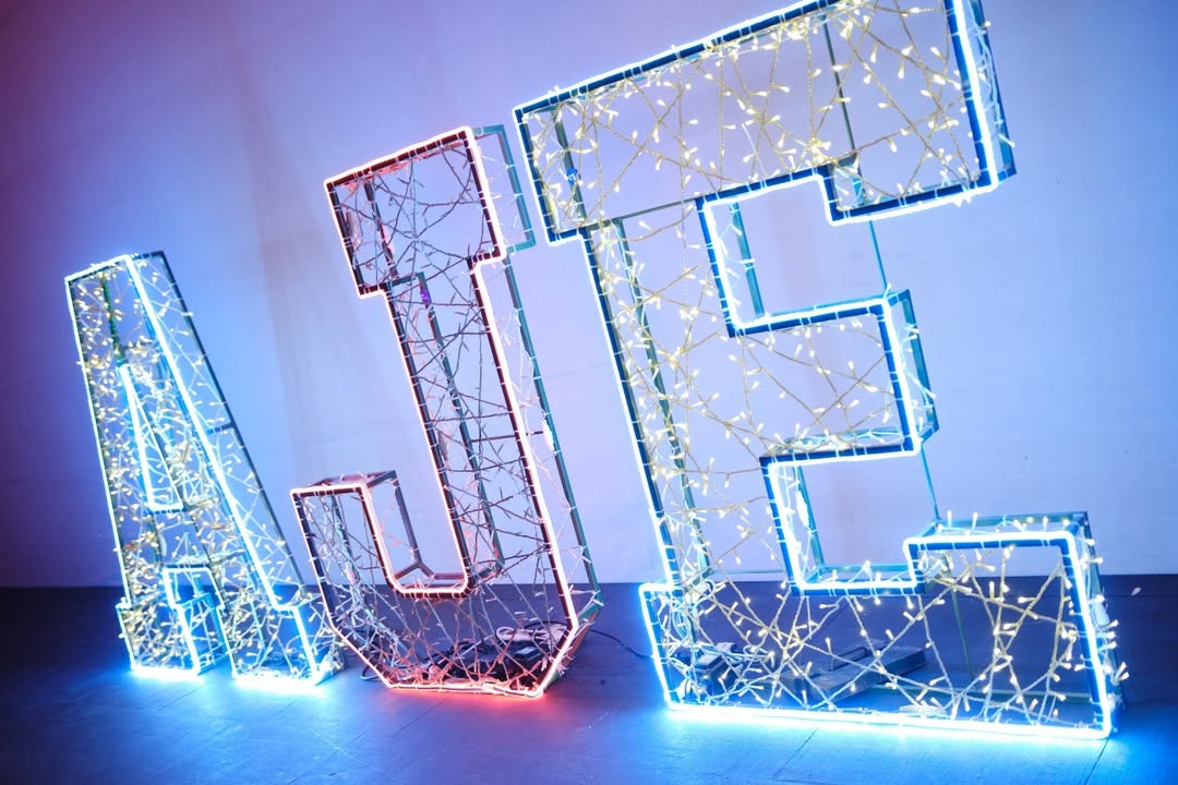 Letras luminosas AJE decoradas con luces LED de colores azul, rojo y blanco.