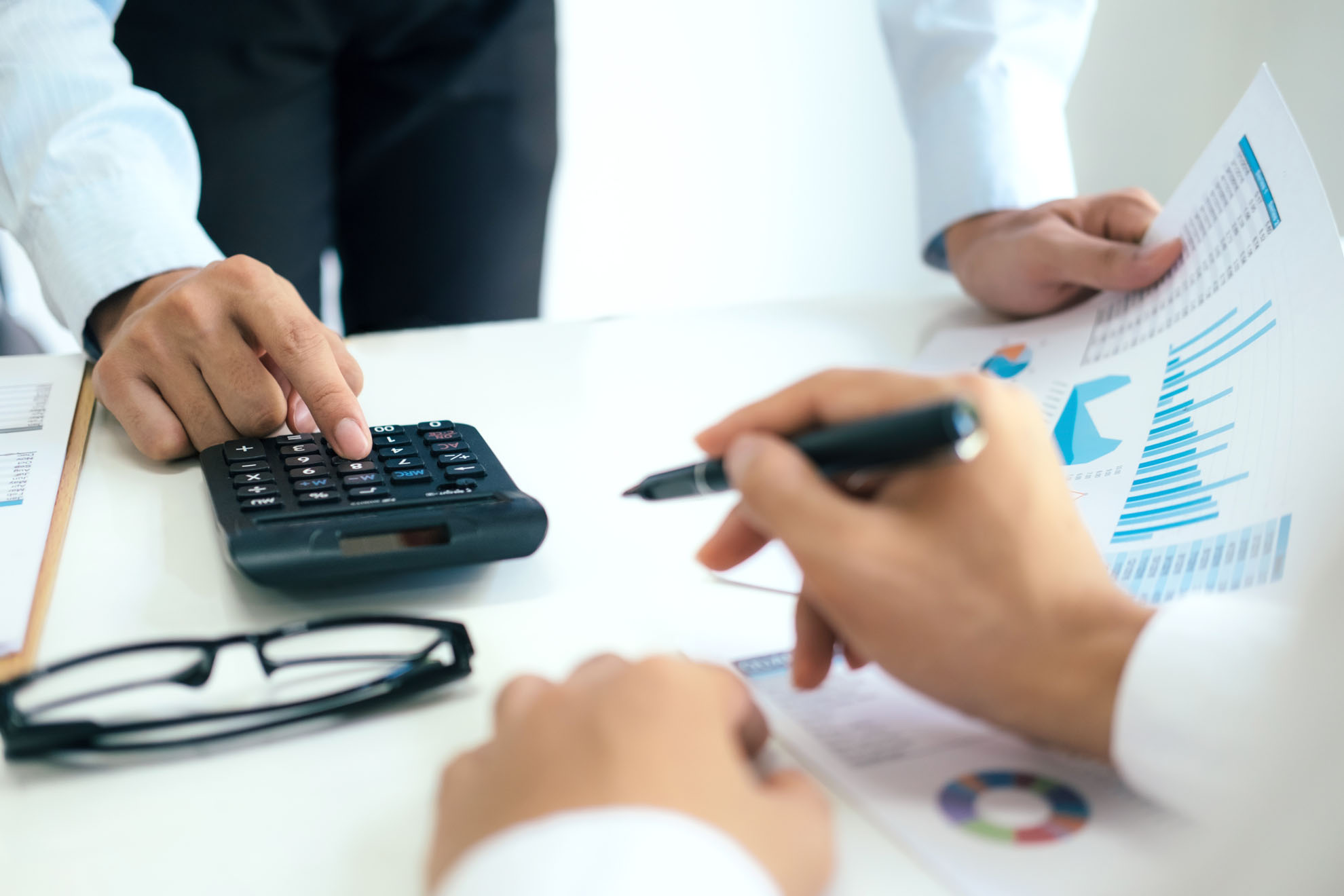 Manos de profesionales revisando gráficos y utilizando una calculadora en una mesa de trabajo.