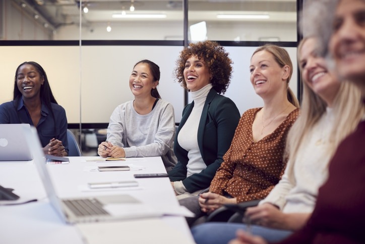 Grupo de mujeres sonrientes participando en una reunión o taller en un entorno profesional moderno.