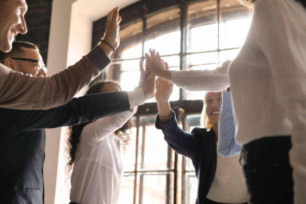 Equipo de personas dando un "high five" grupal en una oficina iluminada por luz natural.