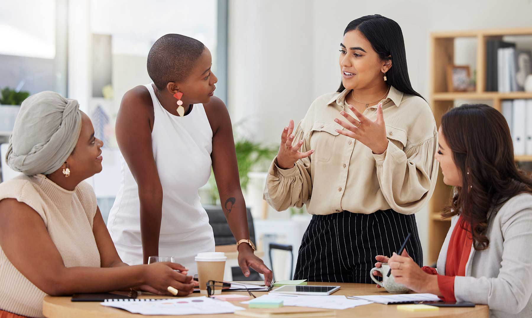 Cuatro mujeres conversan y colaboran activamente en una reunión de trabajo en un entorno de oficina moderno.
