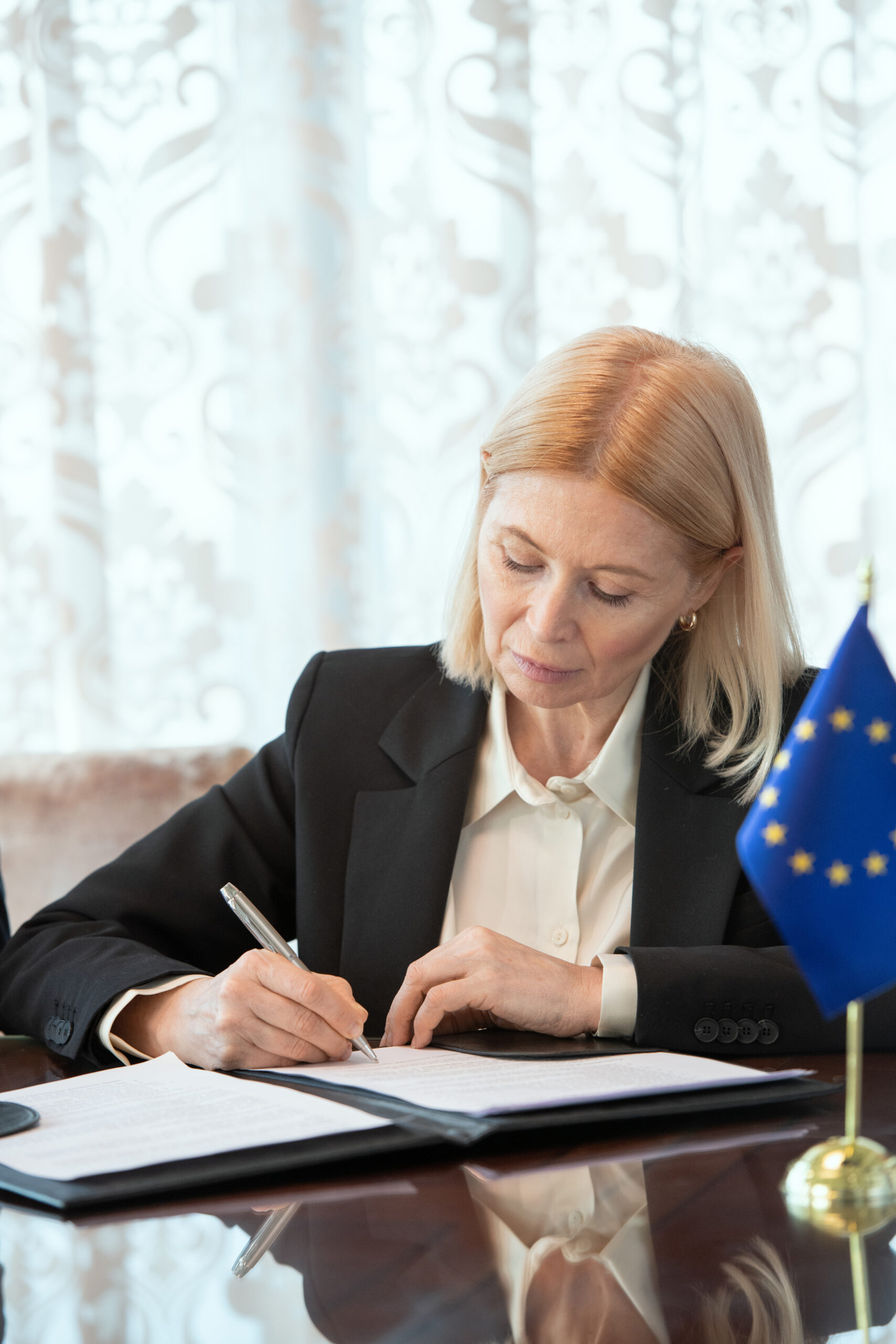 Mujer firmando documentos oficiales junto a la bandera de la Unión Europea, simbolizando la solicitud de financiación europea.